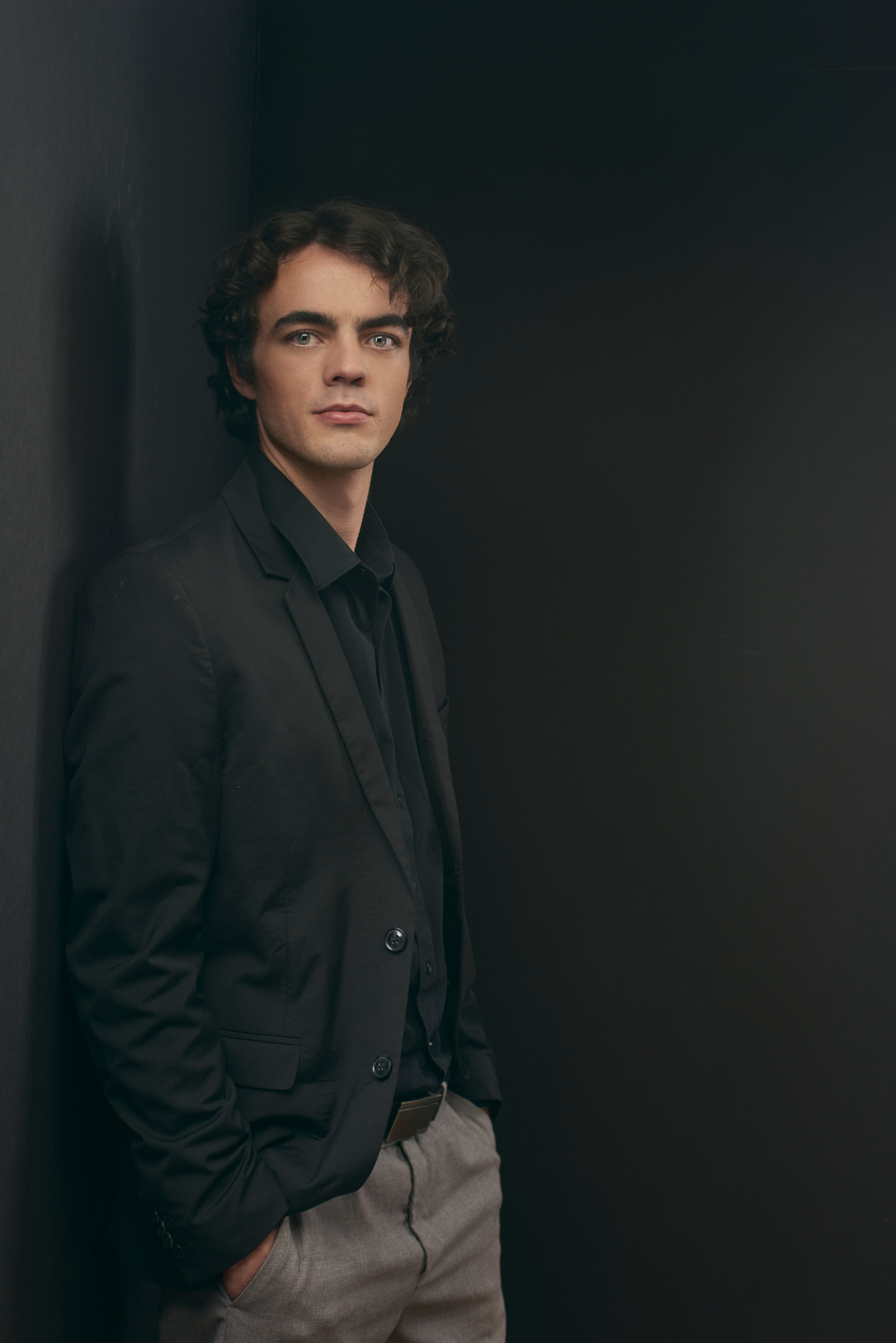 Professional man young man with dark hair wearing black shirt, seated against matching background